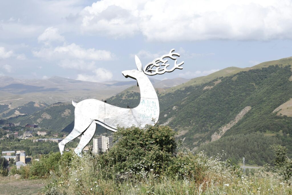Scenic view of a white deer statue overlooking lush green mountains under a cloudy sky.